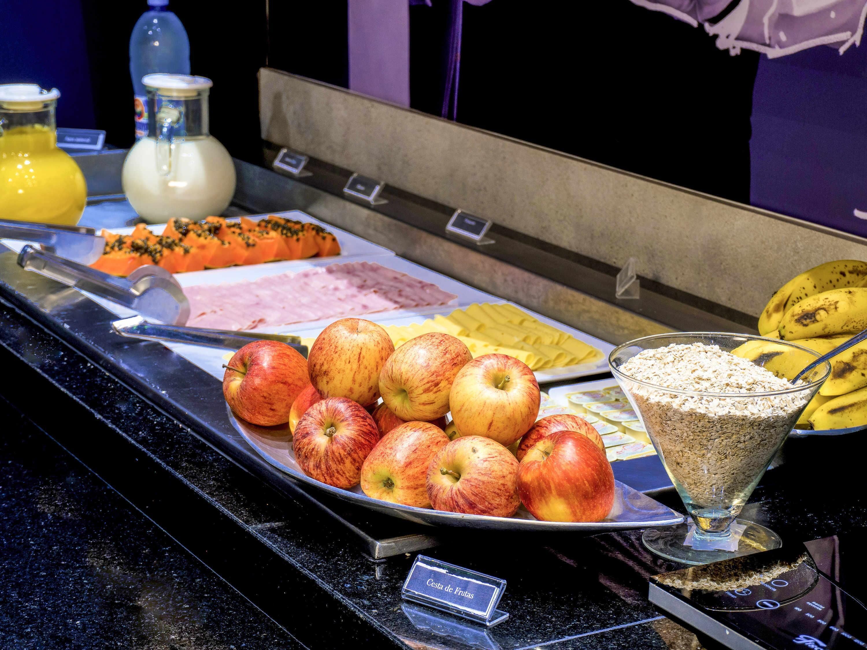 Un buffet proposant des fruits, notamment des pommes et des bananes, ainsi qu’un bol de céréales.