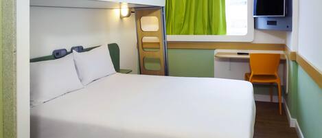 Uma cama beliche com escrivaninha e cadeira, uma televisão e uma janela com cortinas.