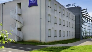 Un bâtiment moderne avec une enseigne « ibis budget » et une autre indiquant « HÔTEL », doté d’un escalier en colimaçon et d’une façade en verre.