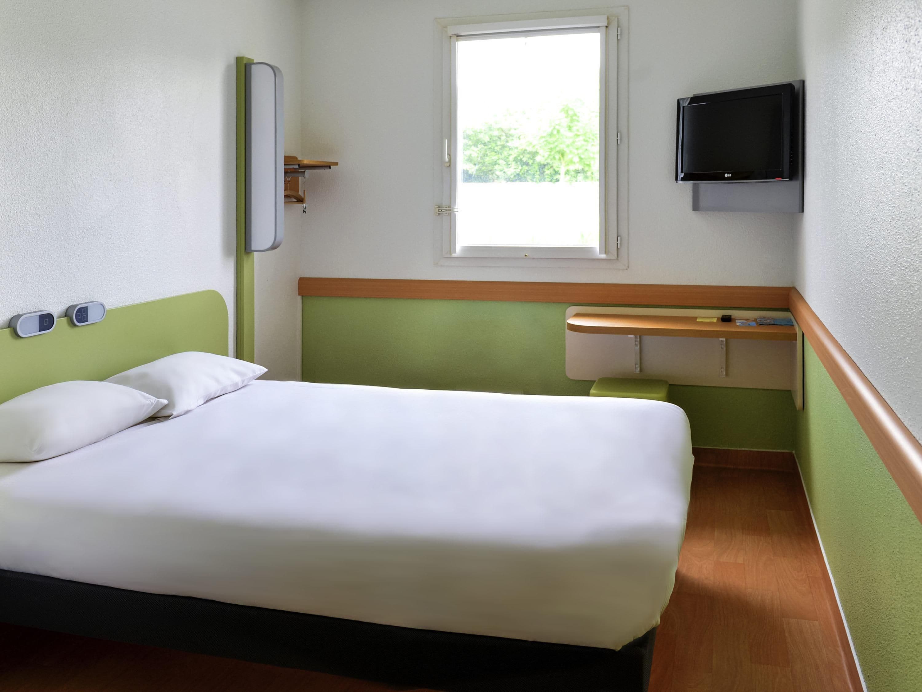 A hotel room with a bed, a television, a window, and a small desk.