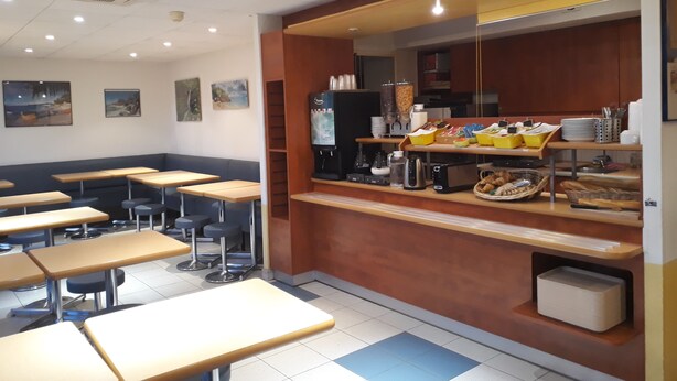 Une cafétéria avec des tables et des bancs, un distributeur de café et un présentoir pour les aliments.