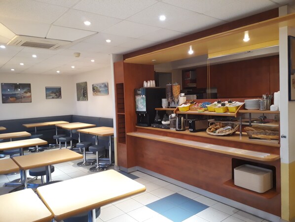 Een cafeteria met tafels en banken, een koffieapparaat en een vitrine met eten.