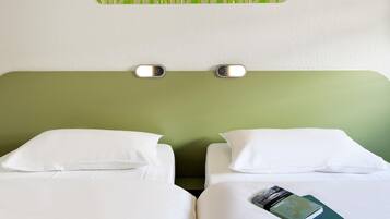 A hotel room with two beds, white bedding, a green headboard, and a wall-mounted light fixture.