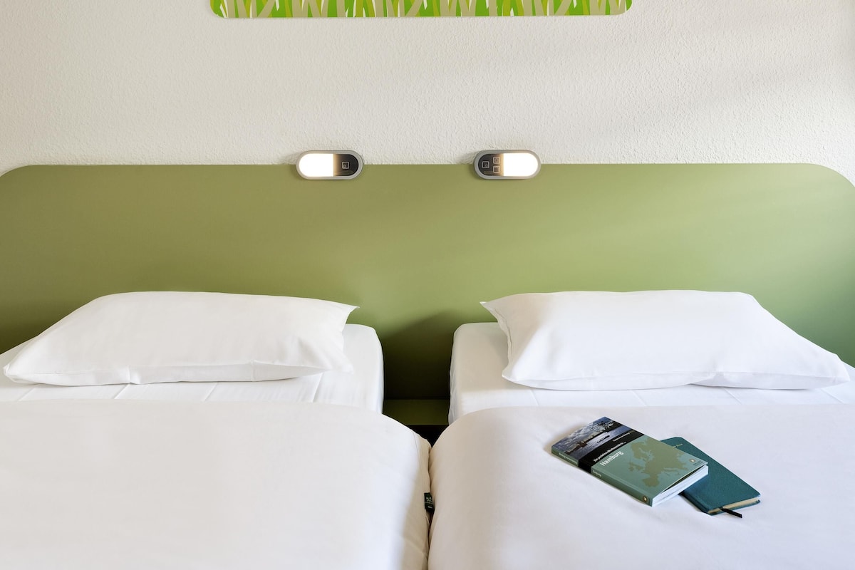 Een hotelkamer met twee bedden, een groen hoofdeinde en een wandlamp.