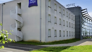 Un bâtiment moderne avec une enseigne « ibis budget » et une autre indiquant « HÔTEL », doté d’un escalier en colimaçon et d’une façade en verre.