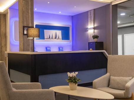 A reception area with a counter, two chairs, a small table with a plant, and a wall-mounted lamp.. ibis budget Ajaccio