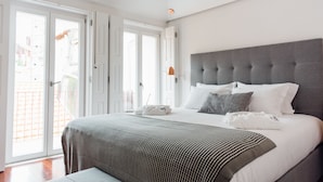 Ein modernes Schlafzimmer mit einem großen Bett, grauem Kopfteil und Blick ins Freie durch die geöffneten Schiebetüren.