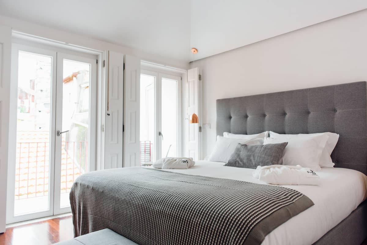 A modern bedroom with a large bed, grey headboard, and a view through the open sliding doors to the outside.