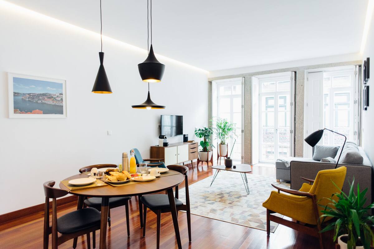 A modern living room with a dining area, featuring a round table, chairs, a sofa, and a TV.