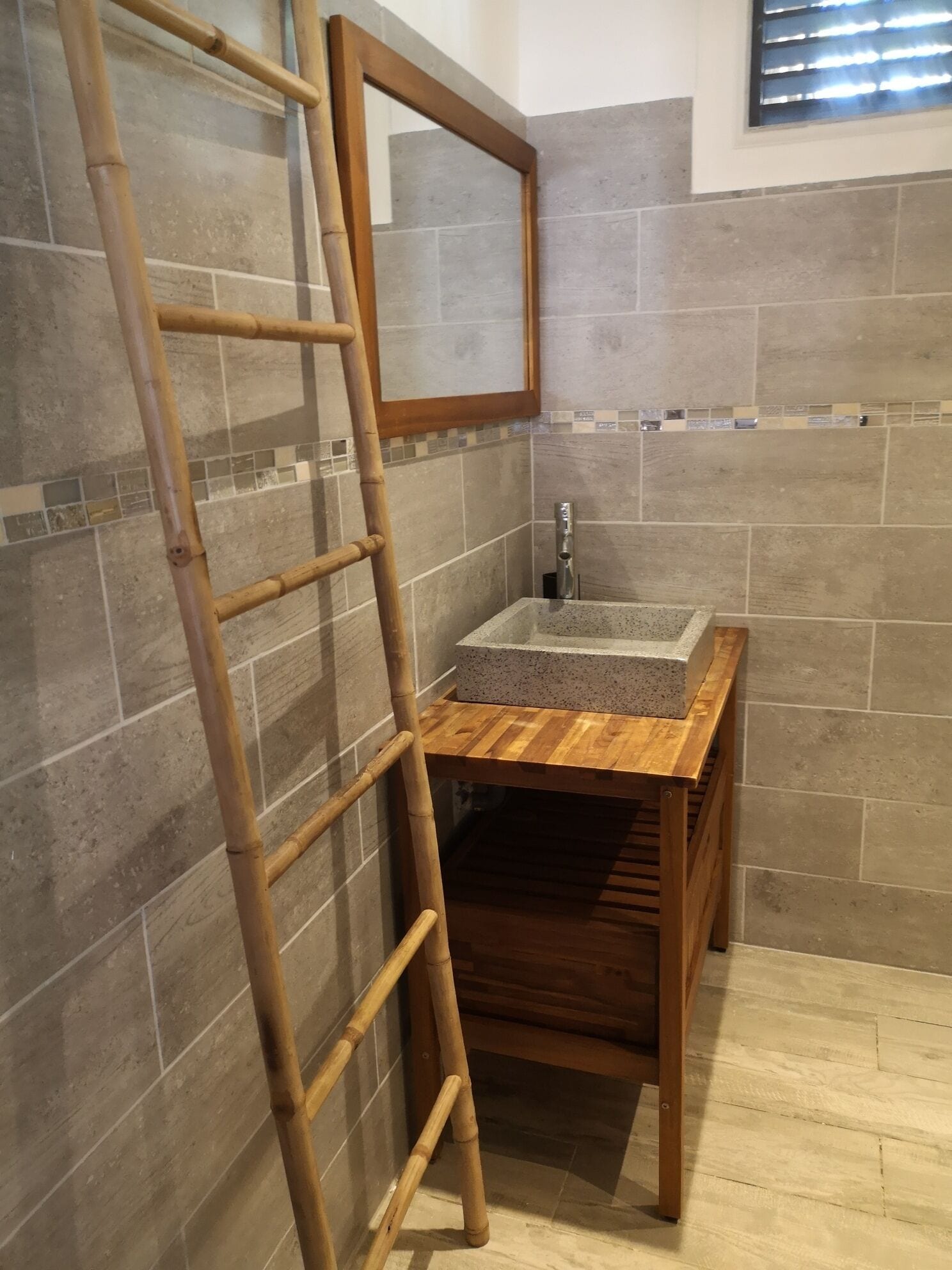 Ein Badezimmer mit einem Holzkosmetikschrank, einem Spiegel und einer gefliesten Rückwand.