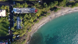 Vue aérienne d’une propriété située sur la côte, avec un ensemble de panneaux solaires, un parking et une plage.