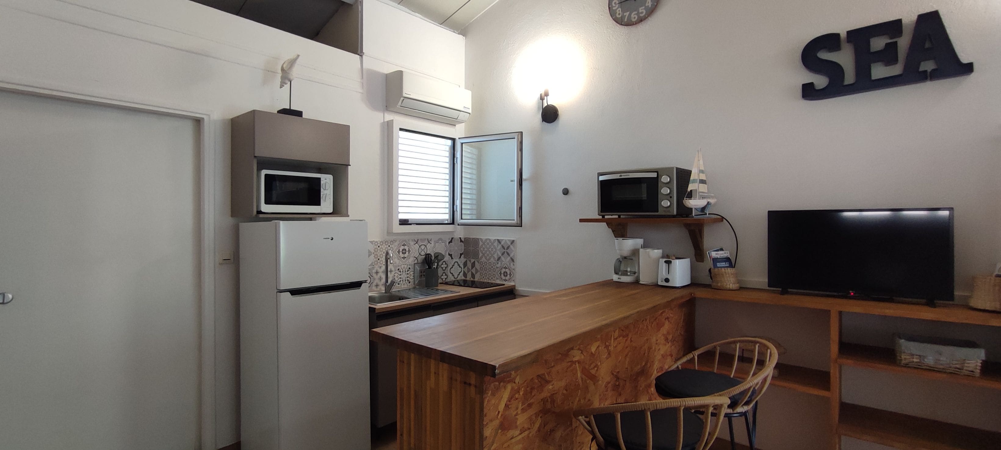 A compact kitchen with a microwave, toaster, and a television on a wooden shelf.