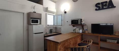 A compact kitchen with a microwave, toaster, and a television on a wooden shelf.