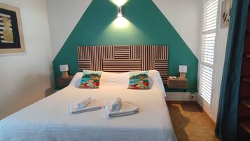A hotel room with a bed, two pillows, a nightstand, a lamp, and a shelf with storage boxes.