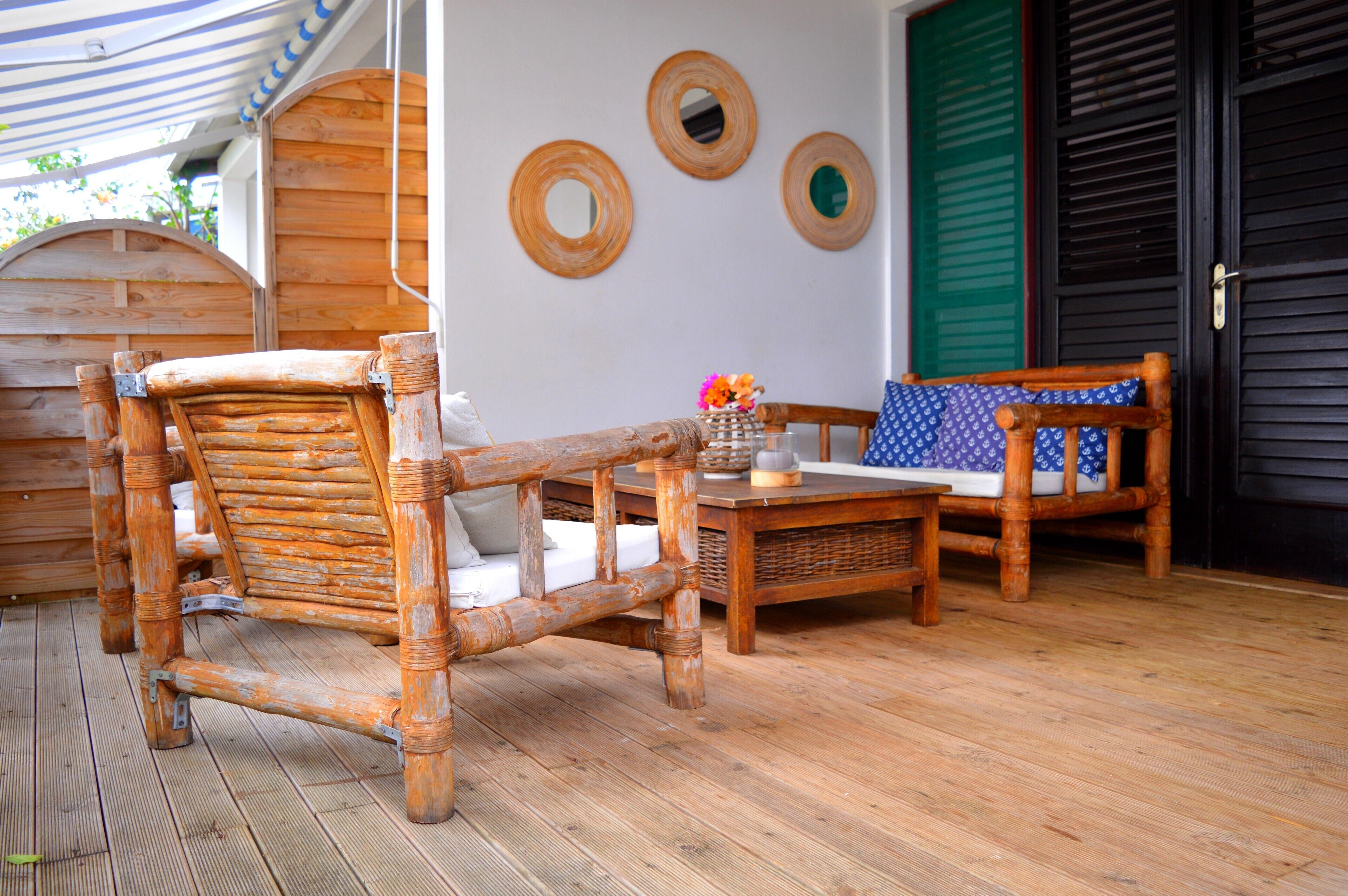 A wooden deck with a rustic bench and a small table, a wicker basket, and a wall with three circular mirrors.
