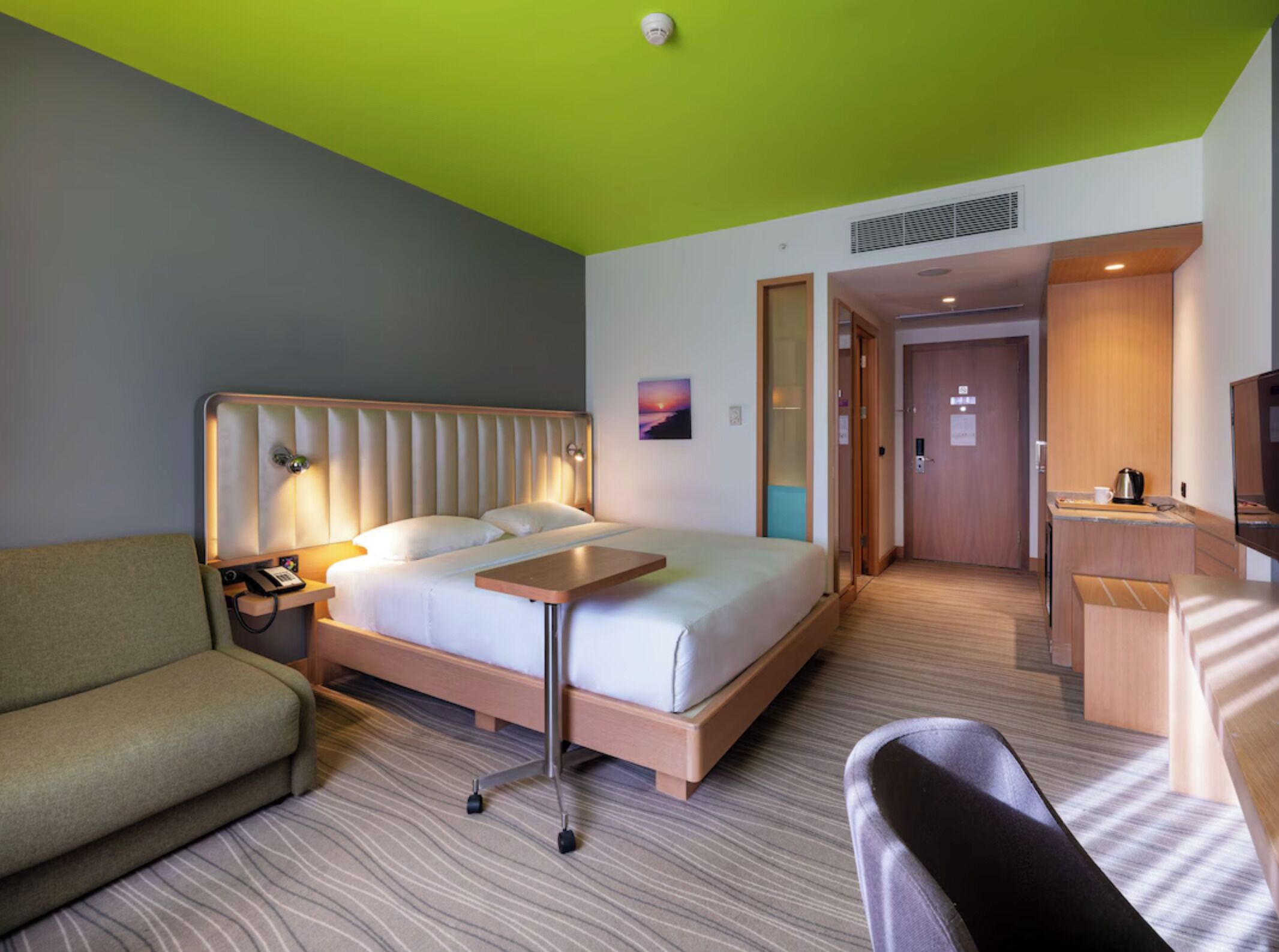 A hotel room with a bed, a desk, a chair, a sofa, and a bathroom door.