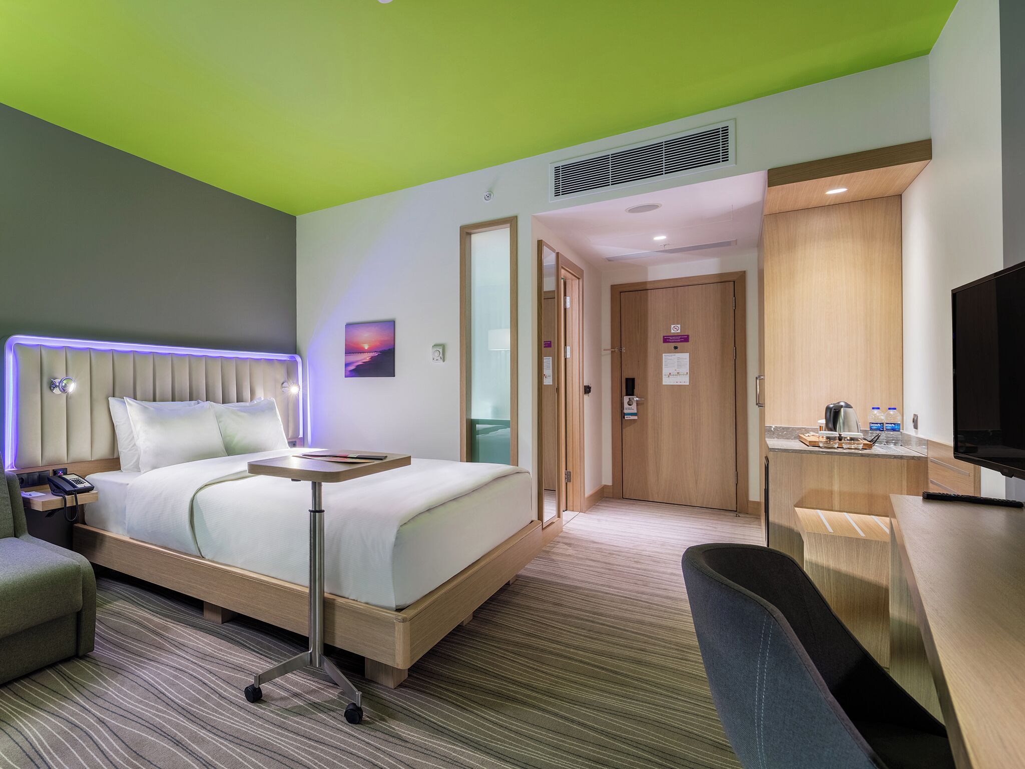 A hotel room with a bed, bedside table, chair, desk, TV, and a bathroom with a shower and toilet.