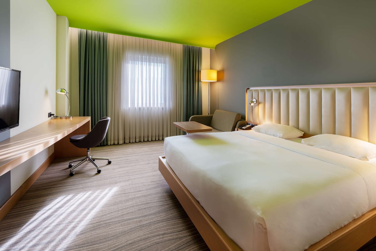 A hotel room with a large bed, a desk with a chair, a television, and a window with curtains.
