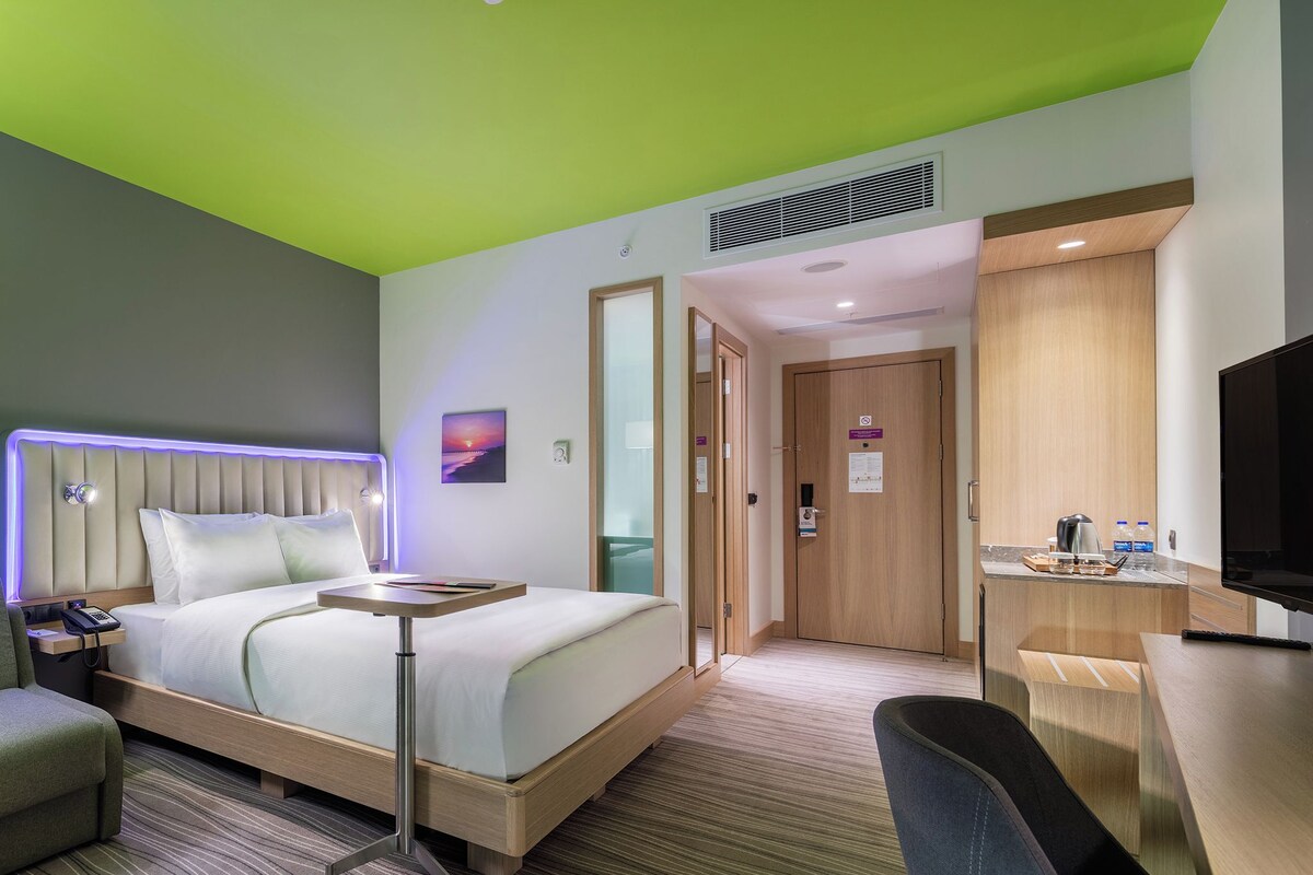 Une chambre d’hôtel comprenant un lit, une table de chevet, une chaise, un bureau, une télévision et une salle de bain avec douche et toilettes.