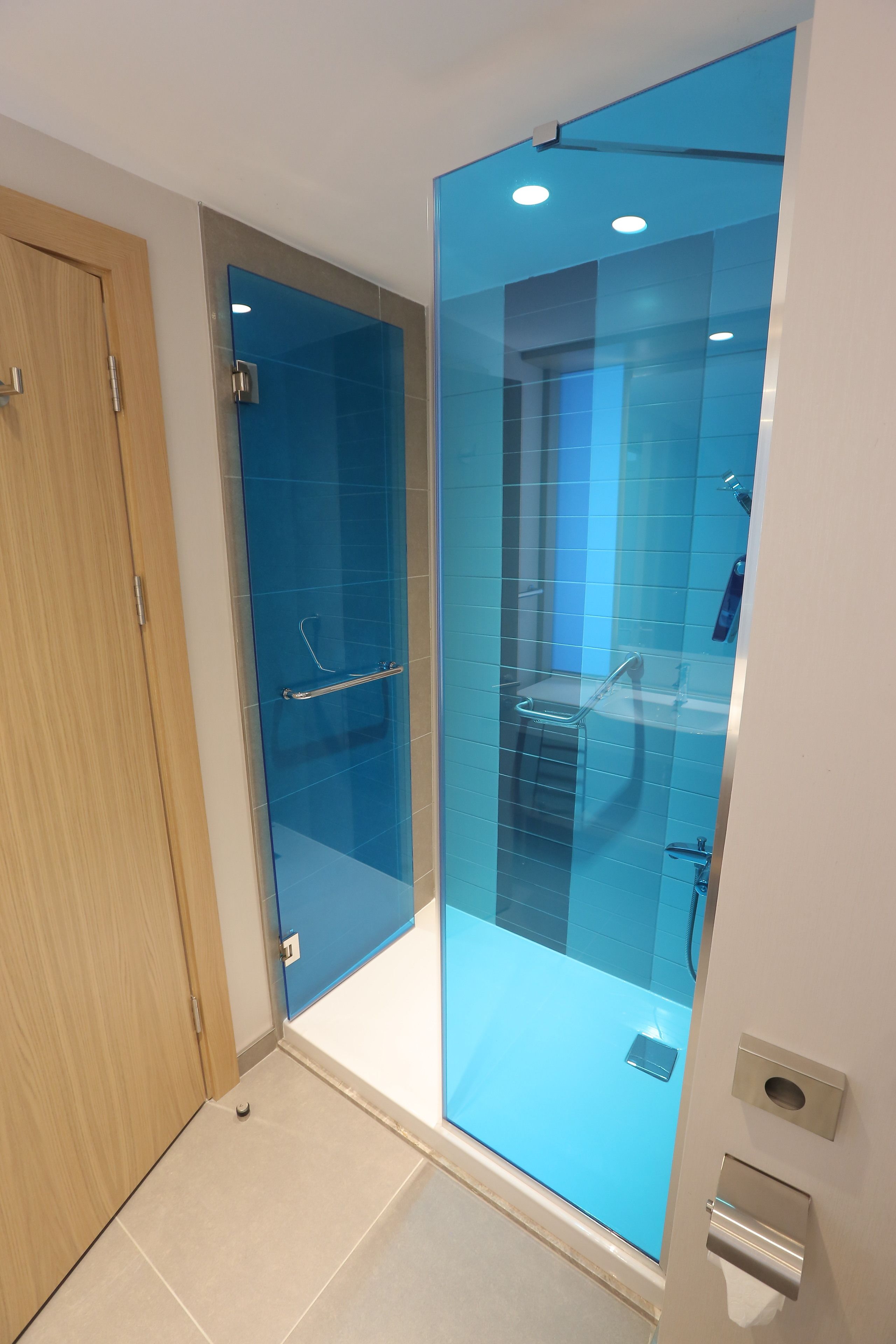 Une salle de bain moderne avec une douche à parois de verre, une porte en bois et un sol carrelé.