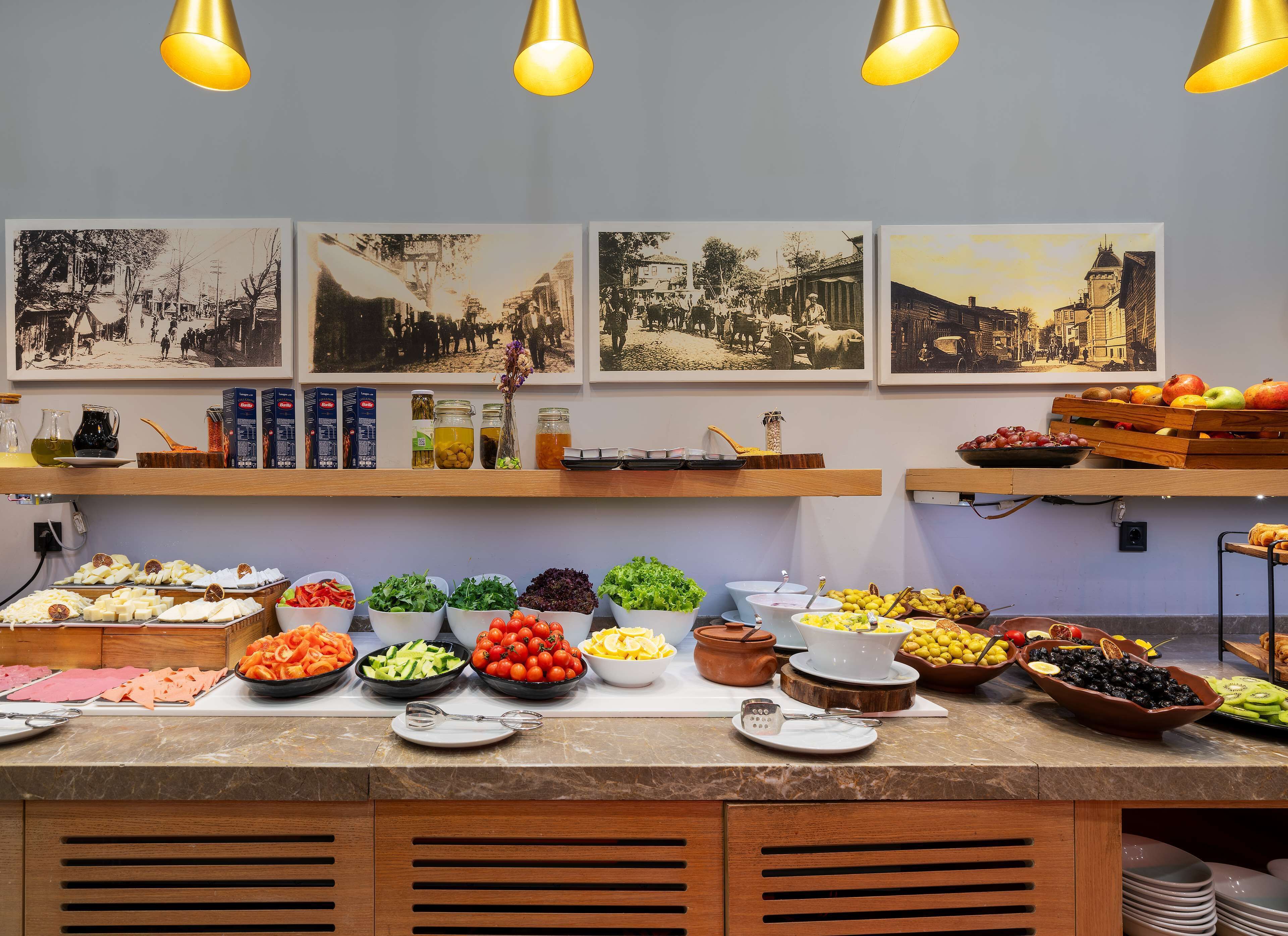 A buffet with various food items and condiments, including fruits, vegetables, and cheeses, displayed on a marble countertop with overhead lighting.