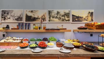 A buffet with various food items and condiments, including fruits, vegetables, and cheeses, displayed on a marble countertop with overhead lighting.