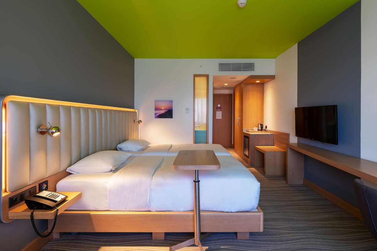 A modern hotel room with a bed, bedside table, lamp, and a TV.