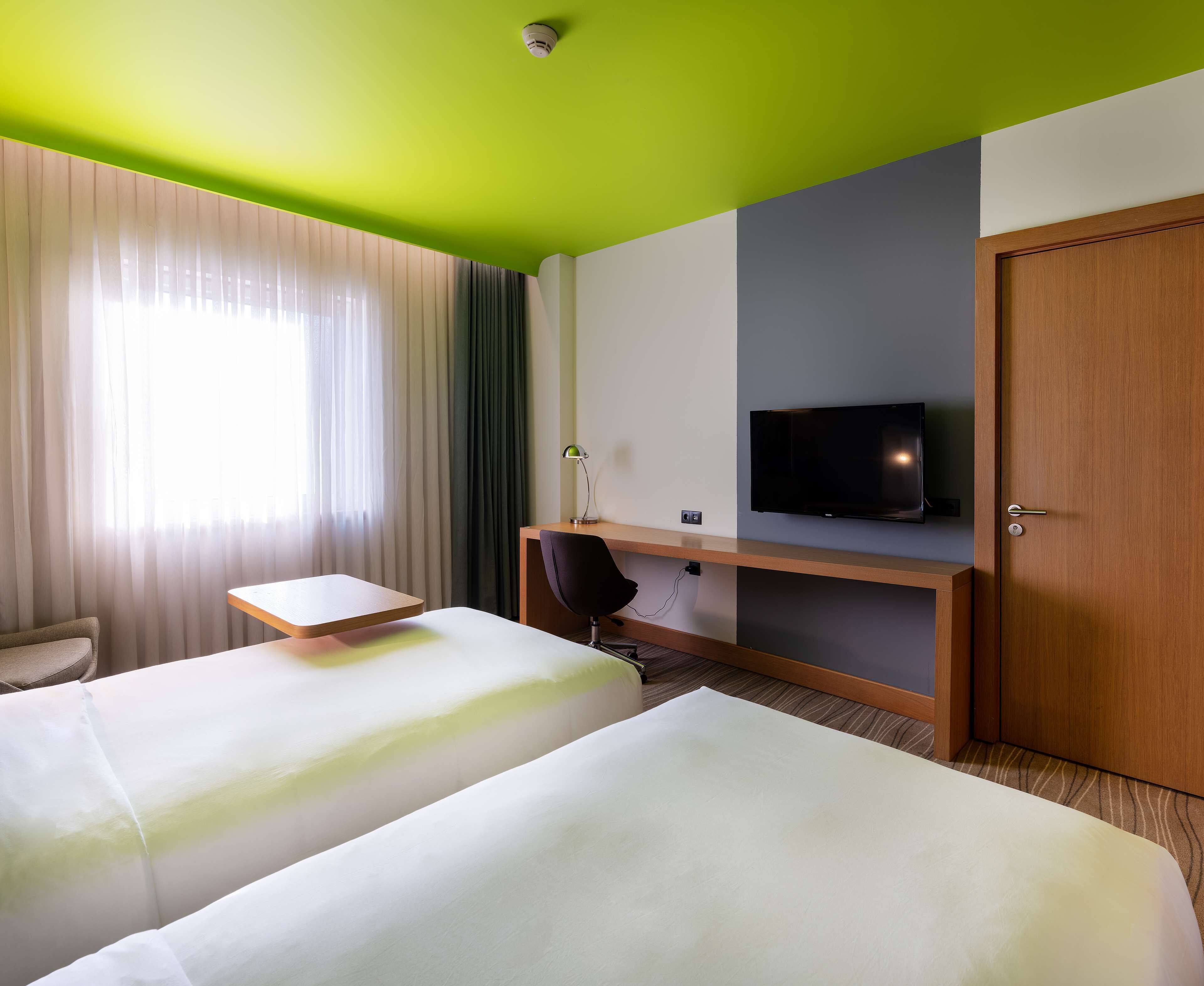A hotel room with two beds, a desk, a television, and a door.