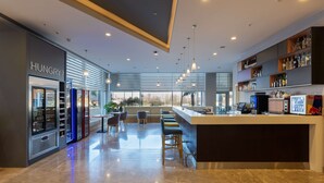 A modern bar area with seating, a vending machine labeled "HUNGRY?", and a minibar with various bottles. - Park Inn by Radisson Samsun (Tekkekoy)