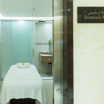 A treatment room with a bed, a small sink, and a mirror.