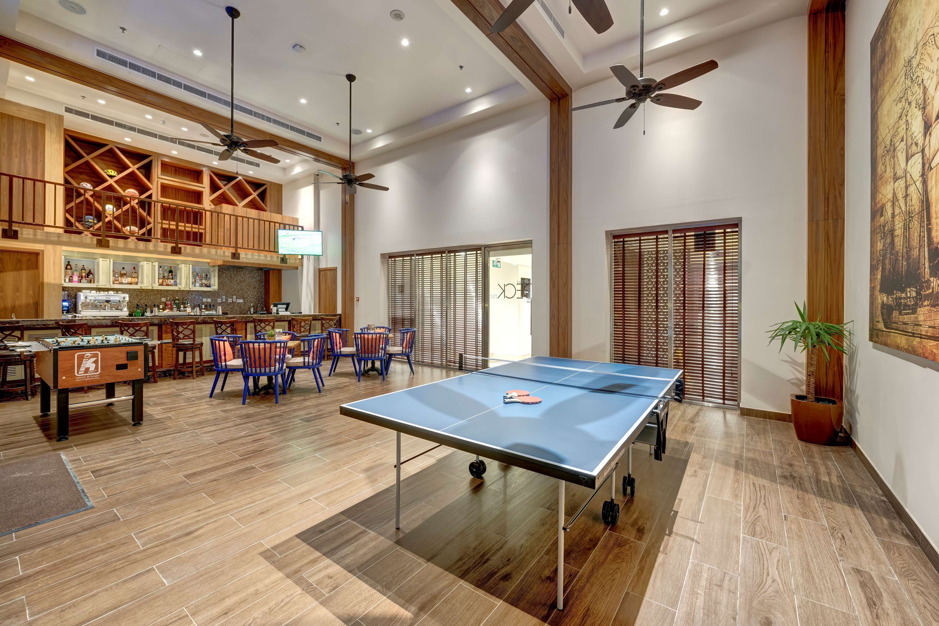 A spacious indoor area with a ping pong table, a foosball table, and a bar area with a television.