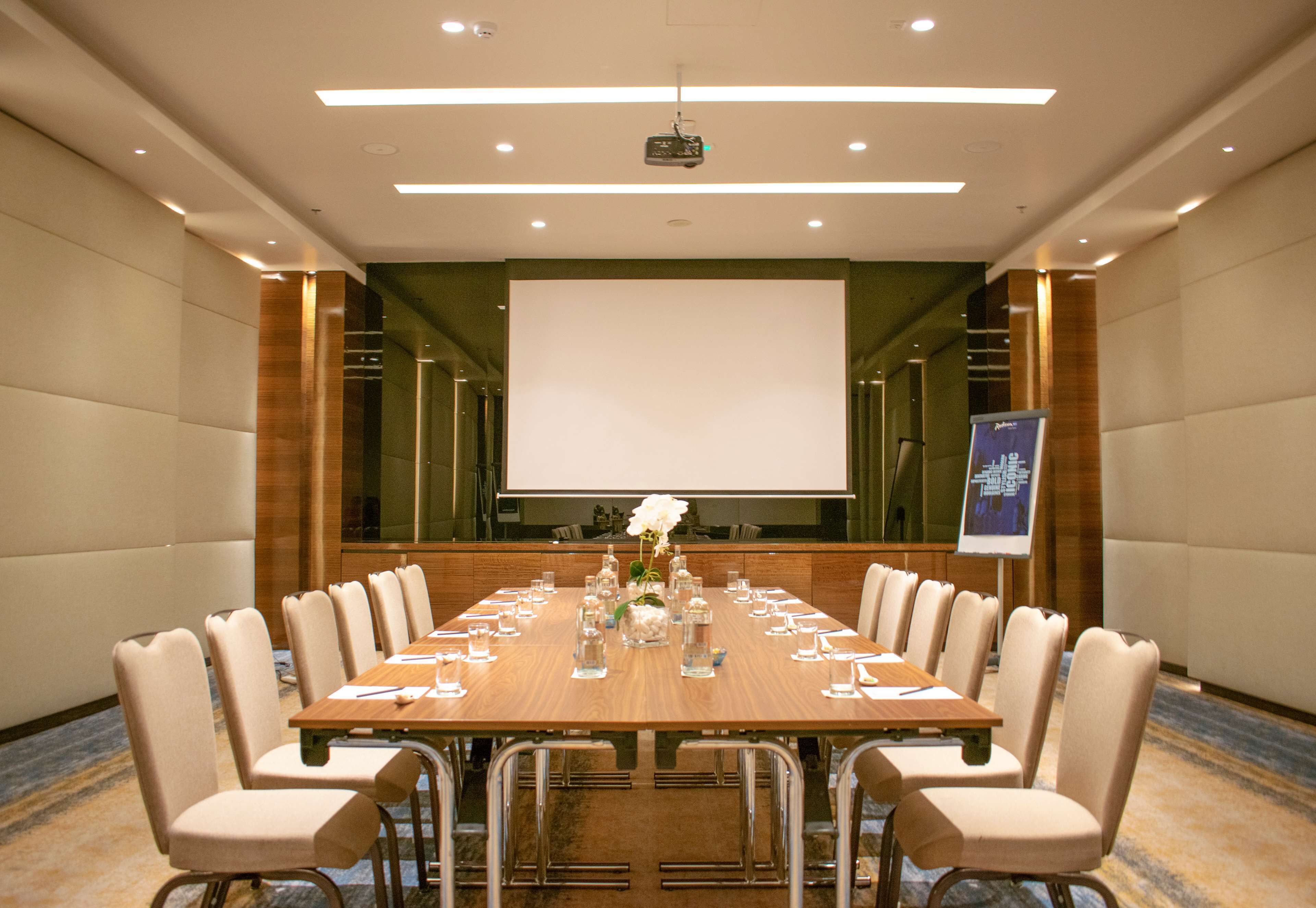A conference room with a long table, chairs, a projector screen, and a floral arrangement.