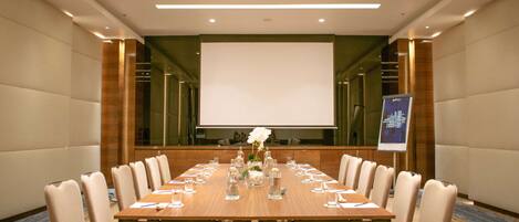 A conference room with a long table, chairs, a projector screen, and a floral arrangement.