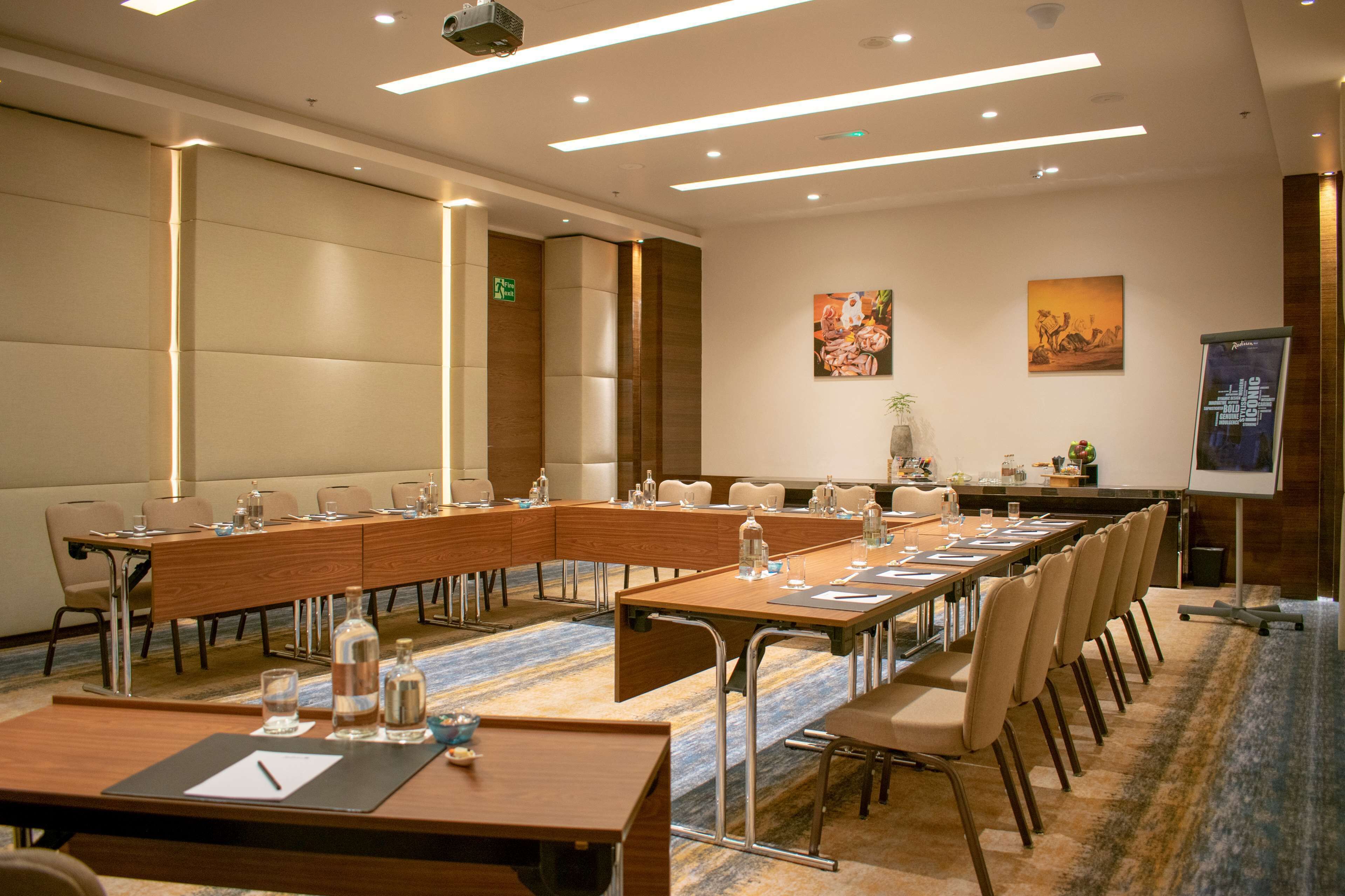 A conference room with a long table, chairs, water bottles, and a projector screen.