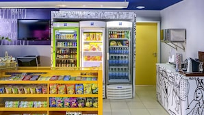 Un puesto de venta de aperitivos con diversas opciones de comida y bebidas envasadas, un televisor y un refrigerador con bebidas.