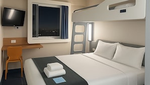 Una habitación de hotel moderna con cama, escritorio, silla, televisor y ventana con cortinas.