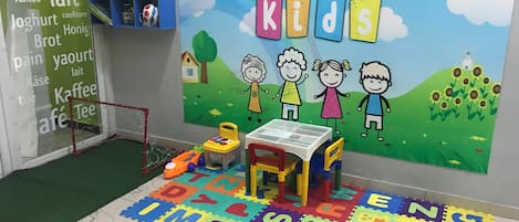 Zona de juegos infantiles con un tapete de alfabeto de colores, una mesita y juguetes.