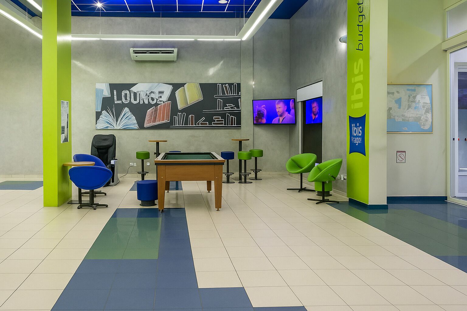 Un área de descanso con mesa de billar, sillas azules y verdes, y un mural en la pared.