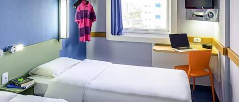 A hotel room with two beds, a desk with a laptop, a TV, and a window with a curtain.