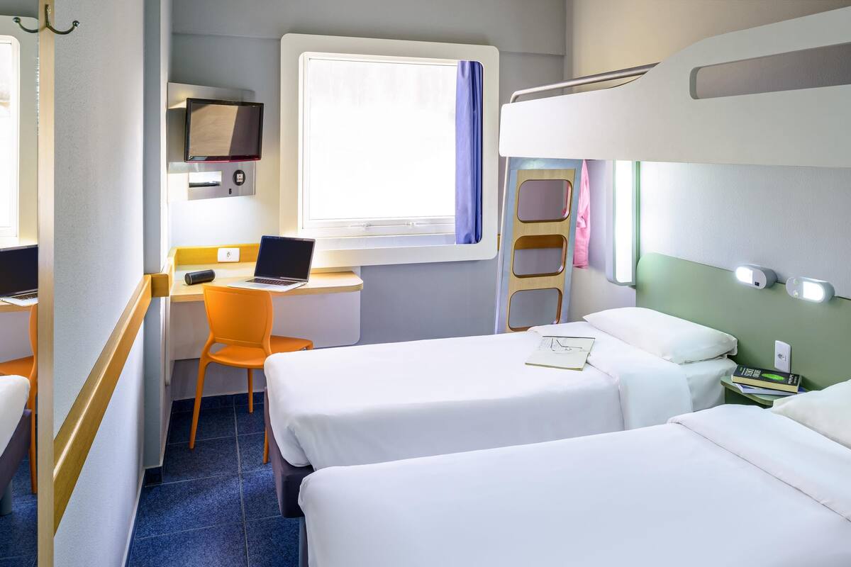 A hotel room with two beds, a desk with a laptop, a chair, and a ladder.