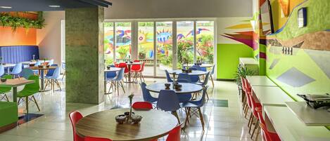 A restaurant with multiple tables and chairs, large windows, and colorful wall art.