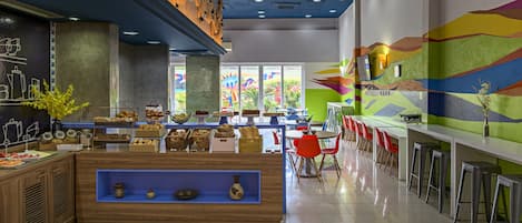 Um café moderno com balcão de madeira, cadeiras vermelhas e um mural colorido na parede.