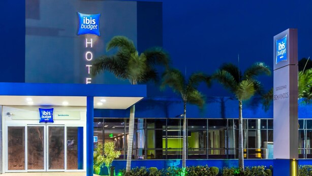 Un hotel ibis budget amb façana moderna, palmeres i entrada ben visible.