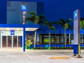 Un hotel ibis budget con fachada moderna, palmeras y una entrada despejada.