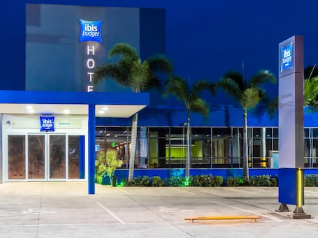 Un hôtel ibis budget doté d’une façade moderne, de palmiers et d’une entrée bien visible.. ibis budget Sertaozinho
