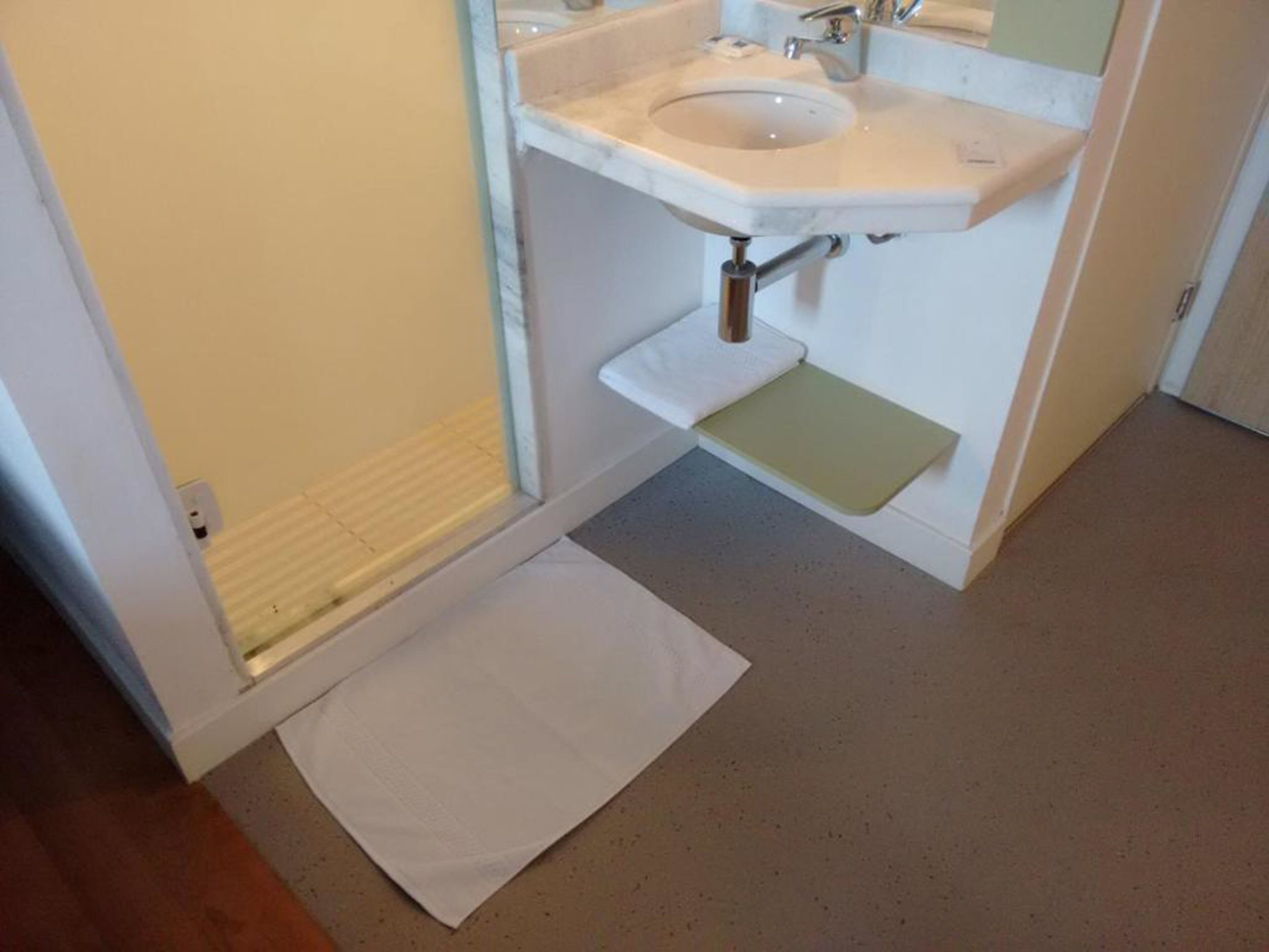 Een badkamer met een witte wastafel, een spiegel en een douchehoek.
