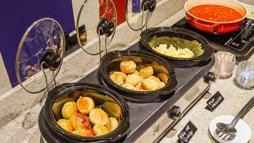 Een keuken met meerdere slowcookers gevuld met verschillende gerechten, een rode pan op het fornuis, en een glas water.