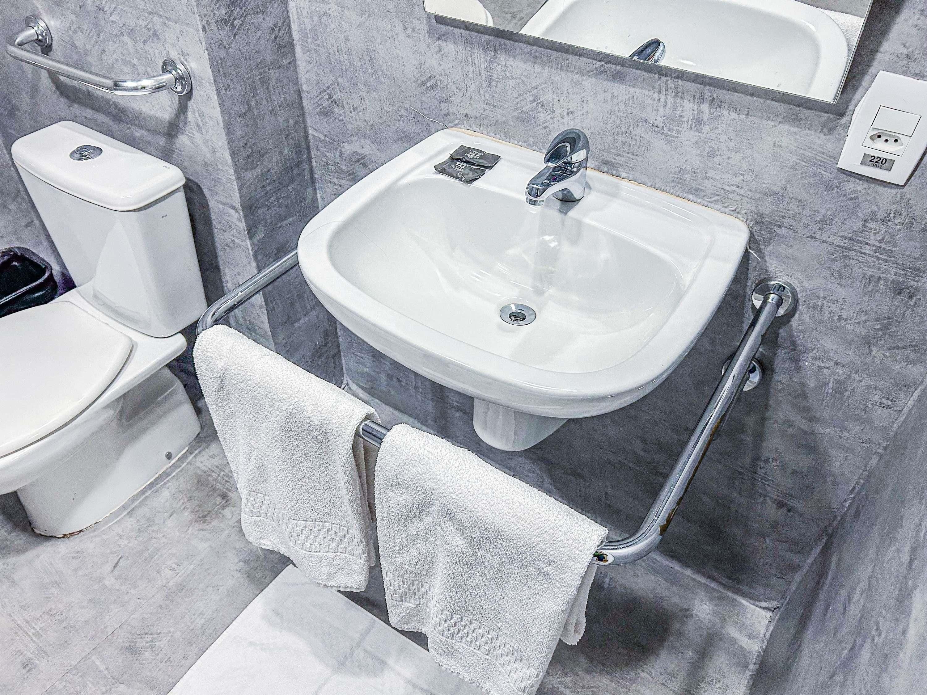 Ein Badezimmer mit einer weißen Toilette, einem Waschbecken mit Spiegel darüber und einem Handtuchhalter mit zwei Handtüchern.