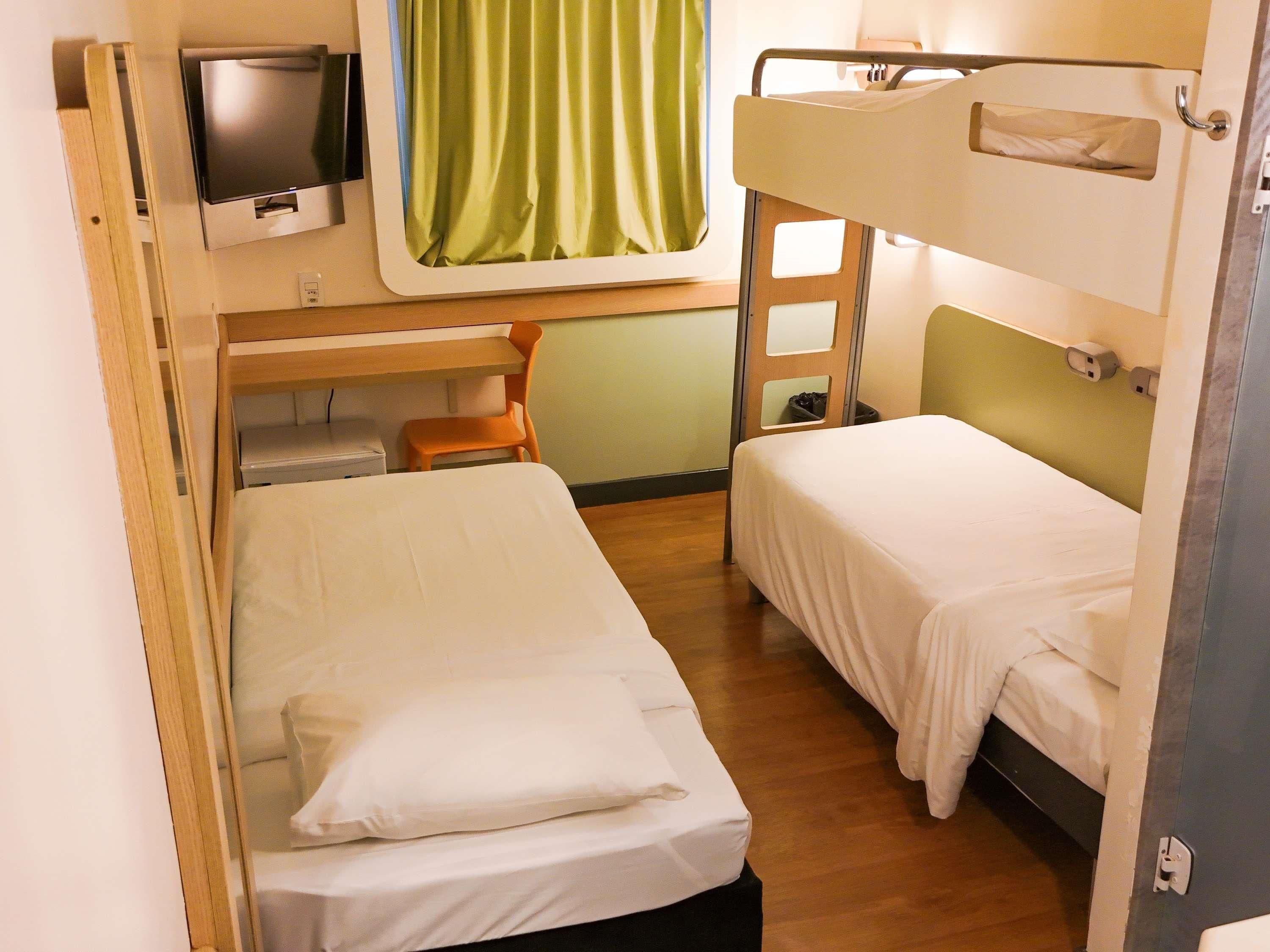 A compact hotel room with bunk beds, a small desk, a chair, and a television.