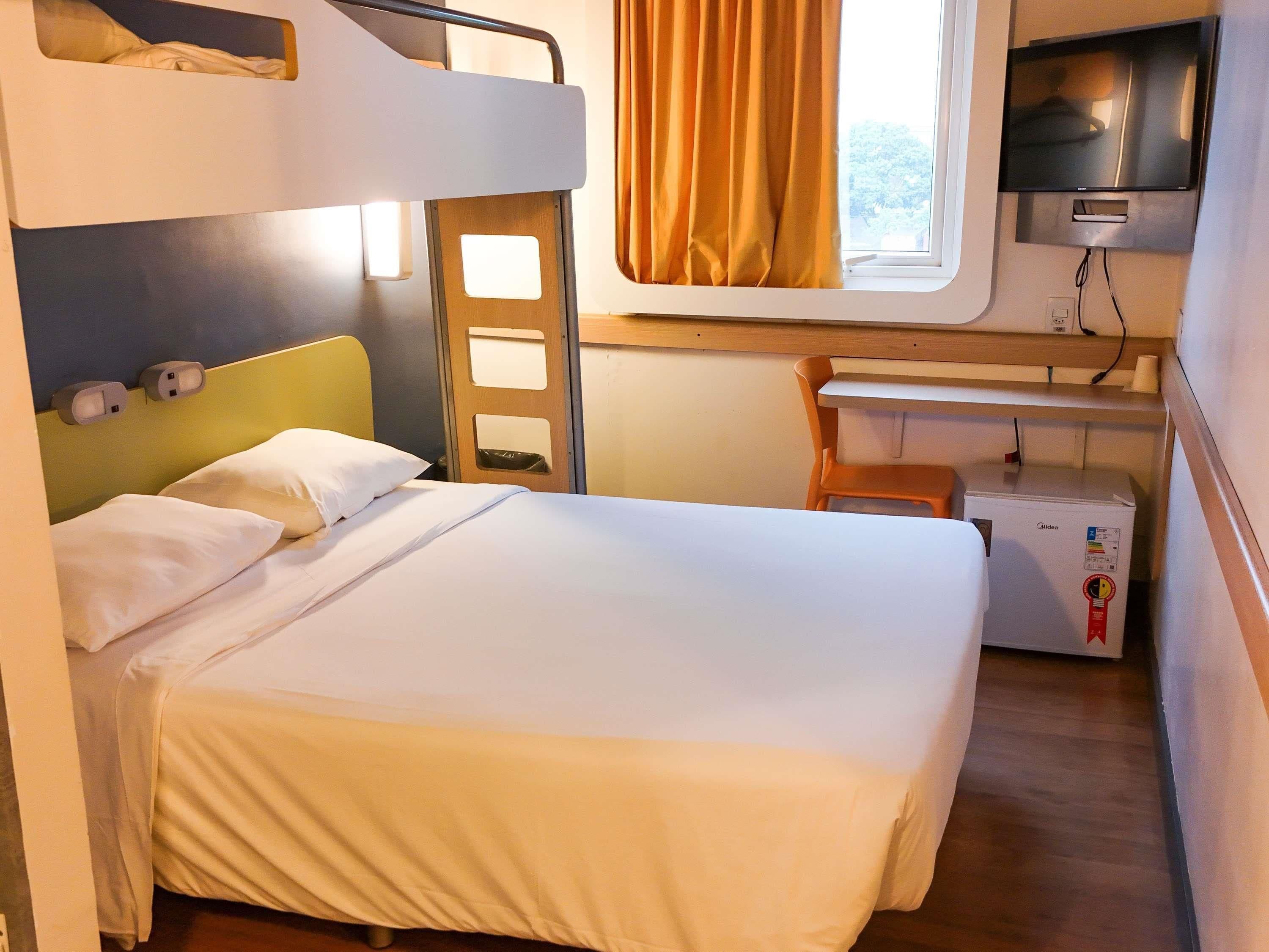A bunk bed with a desk and a refrigerator in a room with a window and curtains.